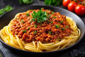 Lentil Bolognese over spaghetti pasta, serve in a black bowl with parsley on top.