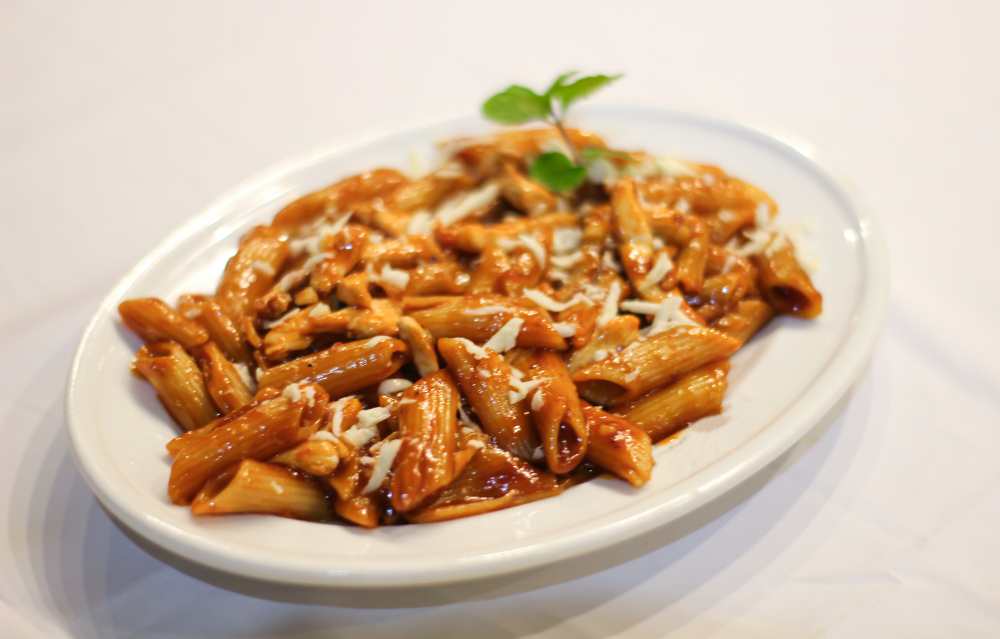 Bbq spicy penne pasta with white sauce top with mint, serve on a white plate