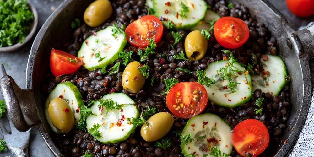 Black lentils salad with cucumber tomato and olives, serve on a black plate.
