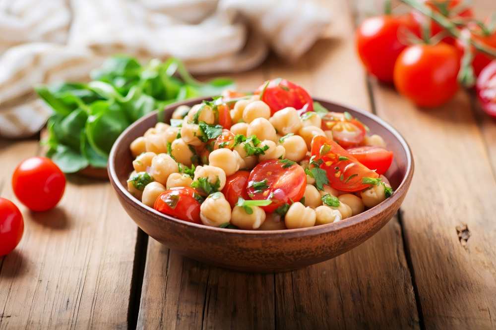 Chickpea salad with fresh cherry tomatoes top with basil , serve in a bowl on a wooden table