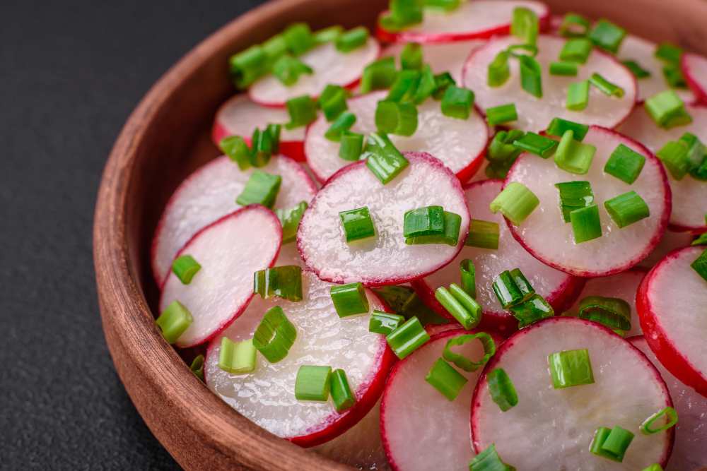 Delicious fresh salad of sliced radishes with green onions, salt and olive oil serve in wooden bowl