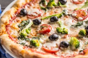 Italian pizza with broccoli spinach tomatoes olives and mozzarela or parmesan cheese. closeup photo