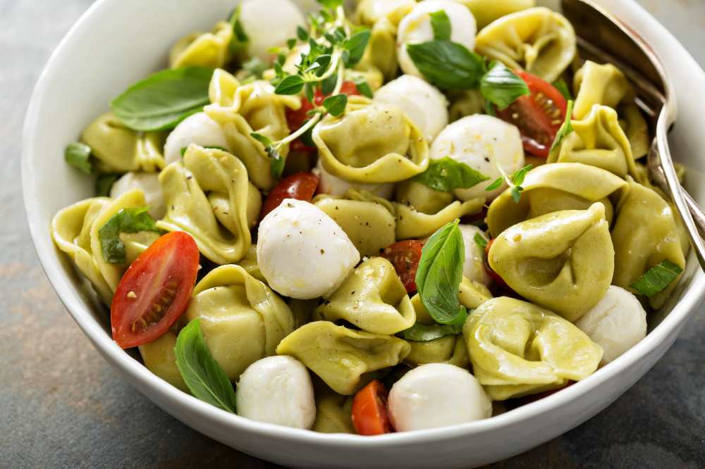 Italian pasta salad with spinach ricotta tortellini , mini mozzarella balls, tomato and basil , serve in a white bowl
