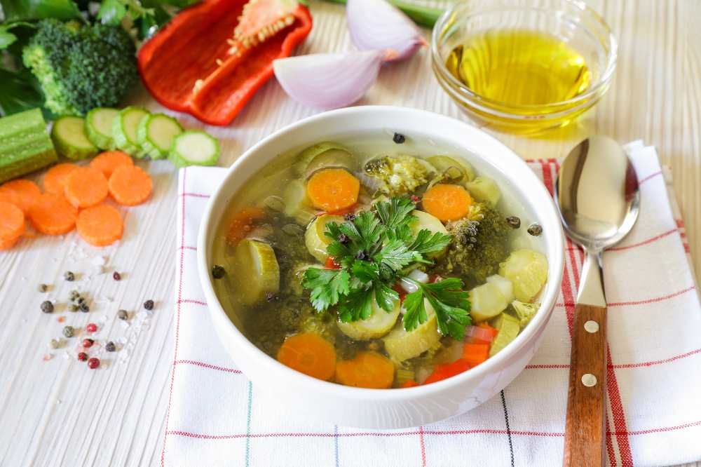 Light Vegetable Soup serve in a white bowl with frash veggie on the side.