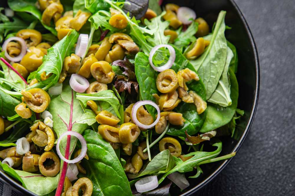 Mix green lettuce leaves, red onion and green olive salad vegetable dish meal food snack on the table rustic black plate top view