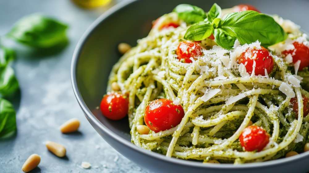pasta dish with pesto and cherry tomatoes top with basil and pine nuts served on a bowl