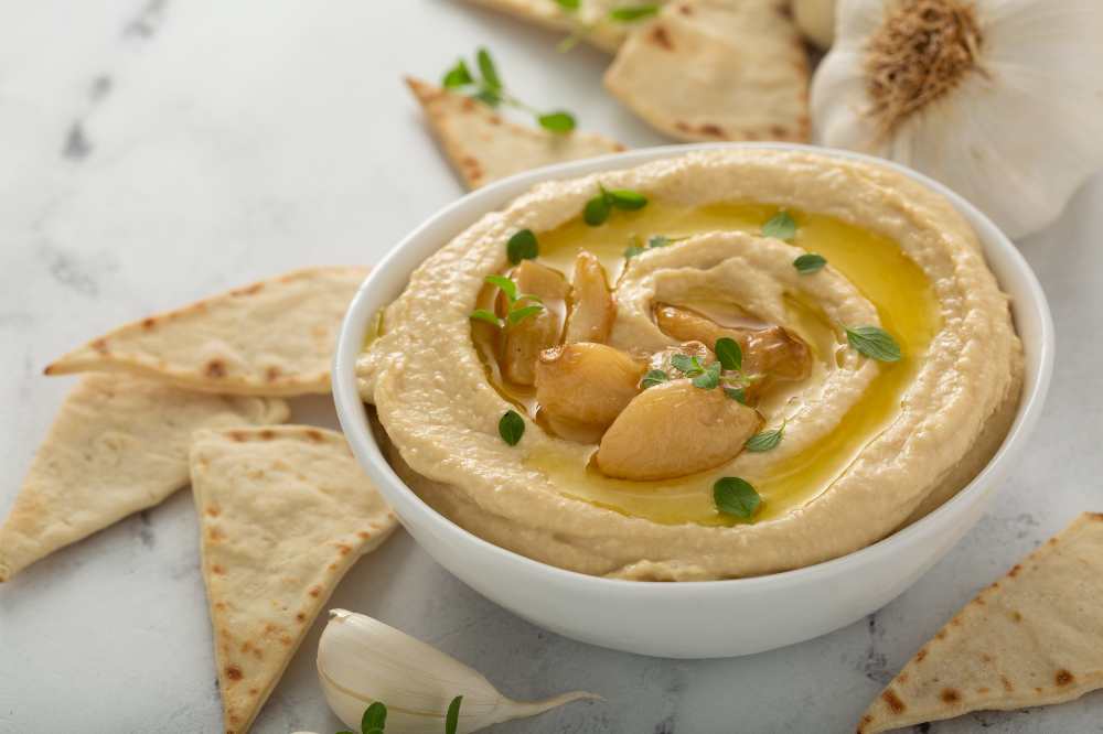 roasted garlic hummus serve in a white bowl with side of pita