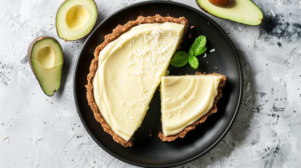 Avocado flour cake pie with coconut topping, serve on a black plate with avocado on the side on a rustic white background