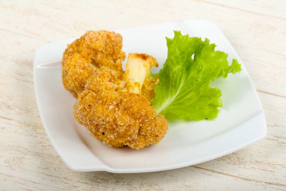 Crispy cauliflower flowers, serve on s small white plate with a green on the side.