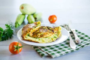 Fried omelet with zucchini, on a wooden table, side of cherry tomato, parsley and zucchini.