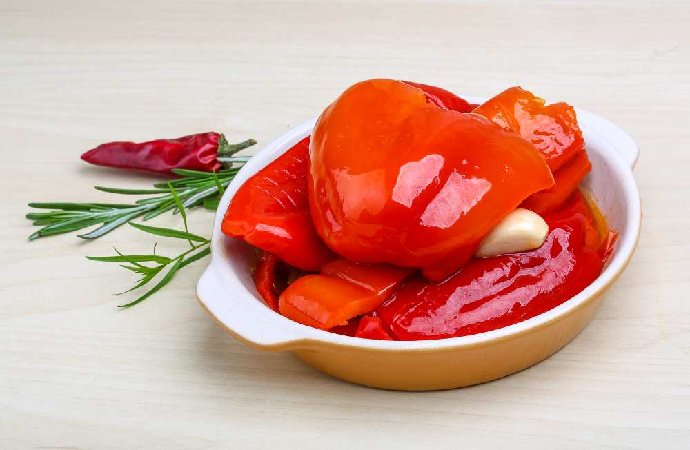 Marinated red pepper with garlic, serve in a white bowl, with rosemary and chili on the side.