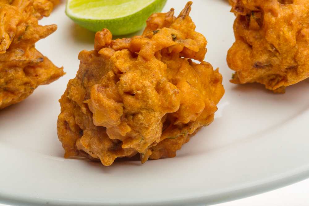 Onion bhajee serve on a white plate with side of lime
