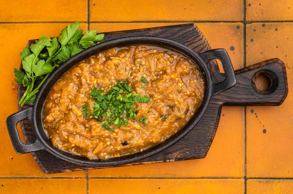 Roasted aubergine ajvar style dip, vegetable spread topped with parsley in cast iron pan on wooden board top view