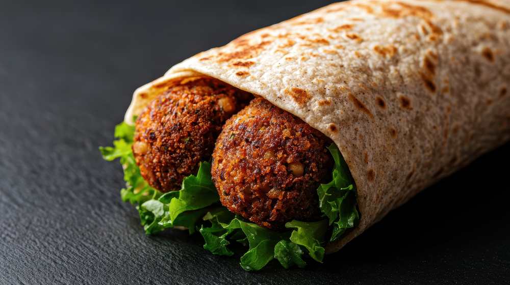 Spicy falafel wrap with lettuce on top of a black counter