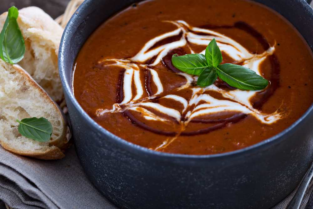 Spicy tomato cream soup, top with white cream and basil, serve in a bowl with bread on the side.
