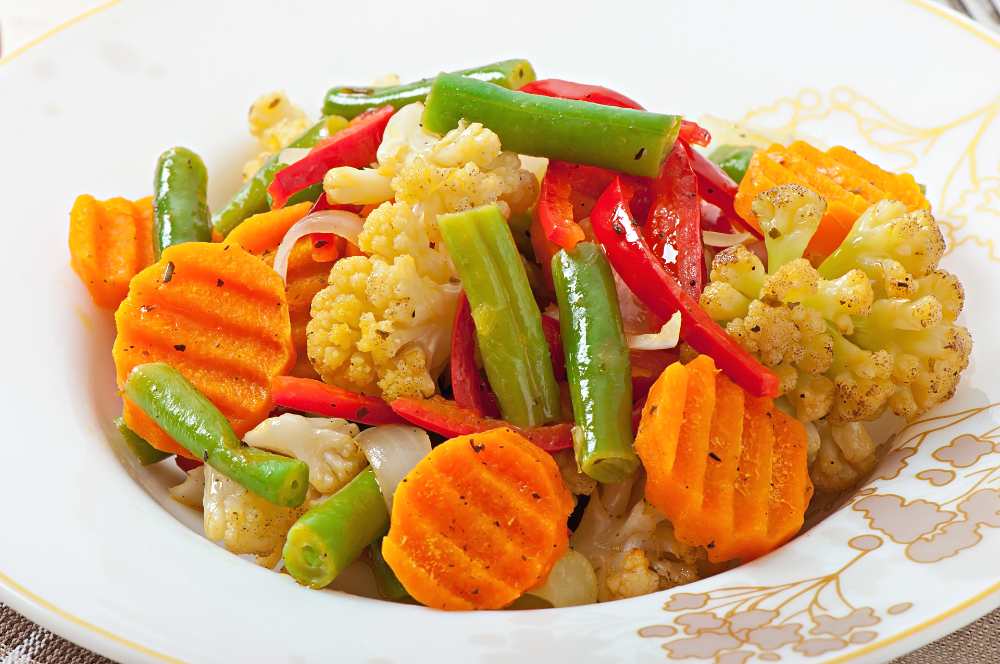 Steamed vegetables -cauliflower, green beans, red pepper, carrots and onions. serve in a white plate, close up view