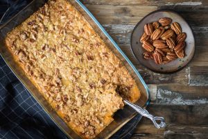 Sweet potato casserole top with pecan crust, serve in a backing dish with side of pecan, top view on a rustic wood.