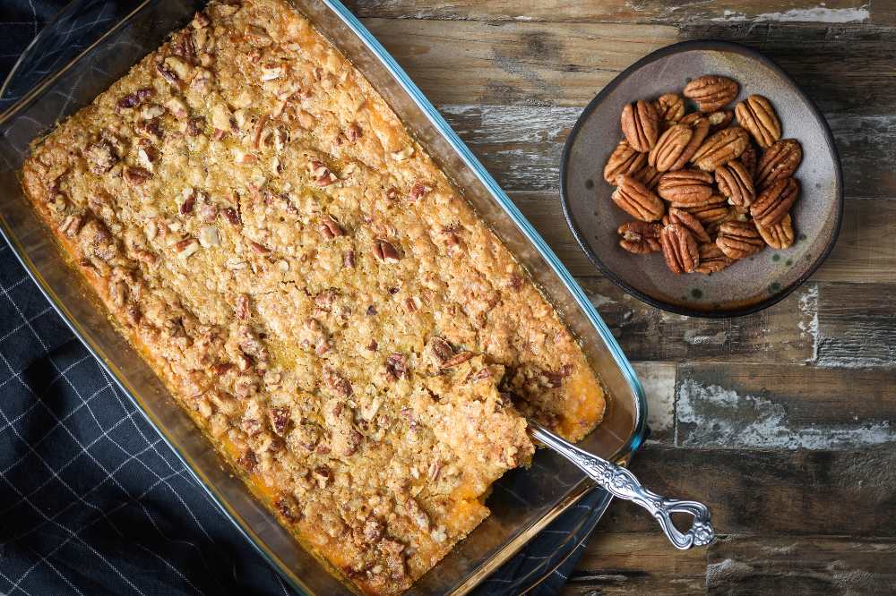 Sweet potato casserole top with pecan crust, serve in a backing dish with side of pecan, top view on a rustic wood.