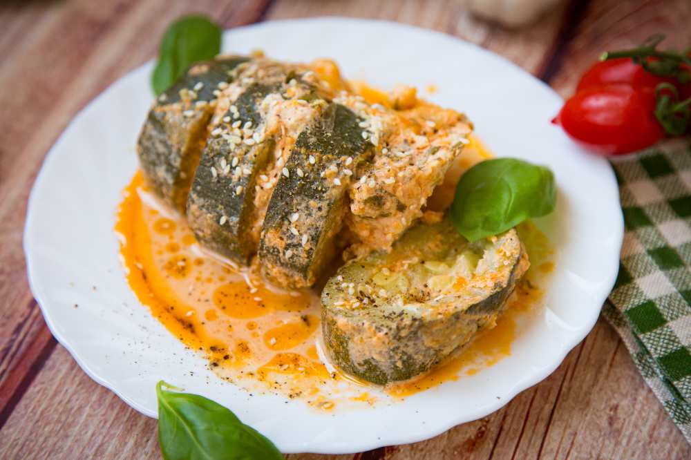 Zucchini pieces in a hot sauce on a white plate with side of whole tomato , on a wooden table.