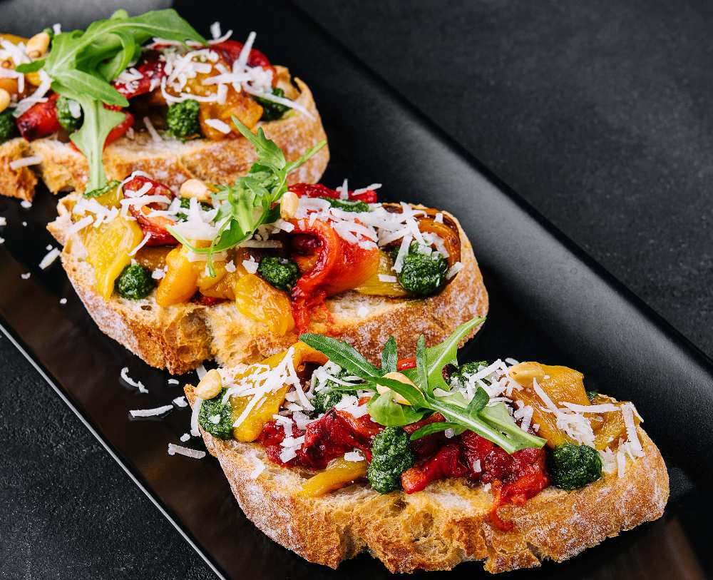 Bruschetta with roasted peppers, pesto, parmesan, and arugula, serve on a black plate