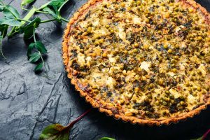 casserole pie with chard and peas serve in a round baking dish dish with green around on a rustic black counter