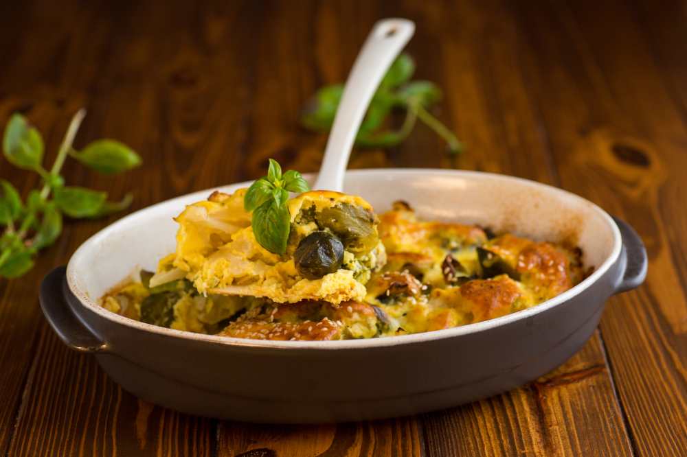 cauliflower and brussels sprouts casserole with cheese, in a ceramic dish on a wooden table