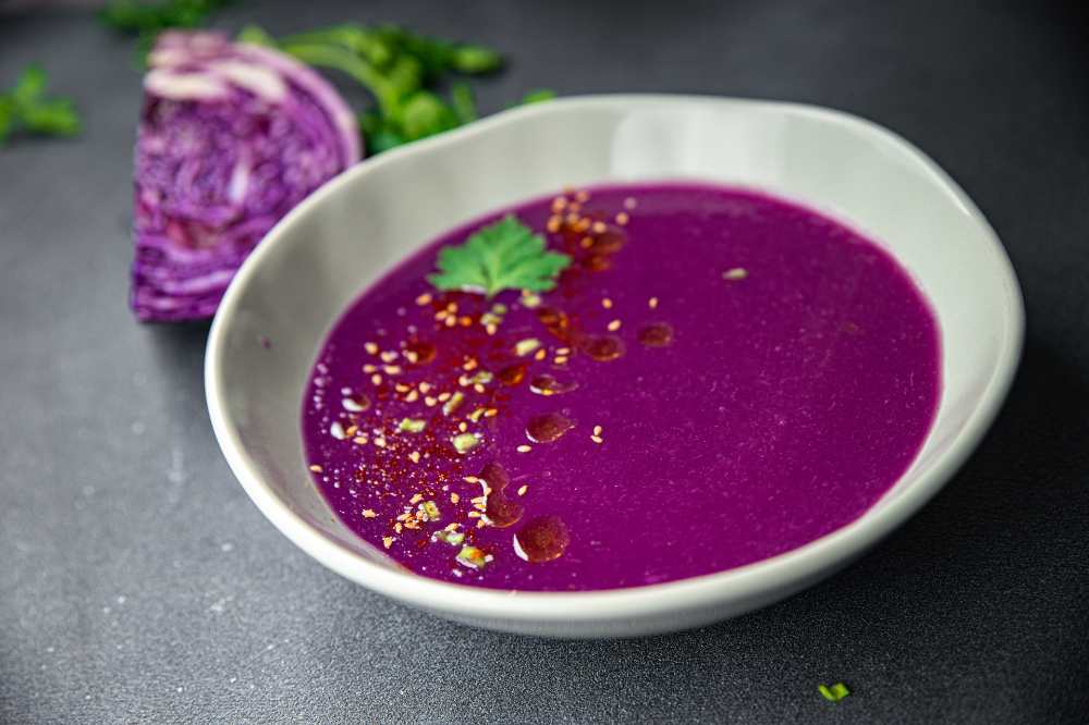creamy red cabbage soup, serve on a black rustic counter and red cabbage on the side
