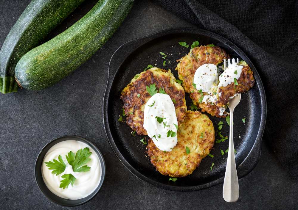 zucchini croquettes top with sour cream and parsley , serve in a black plate with Zucchini and sour cream on the side