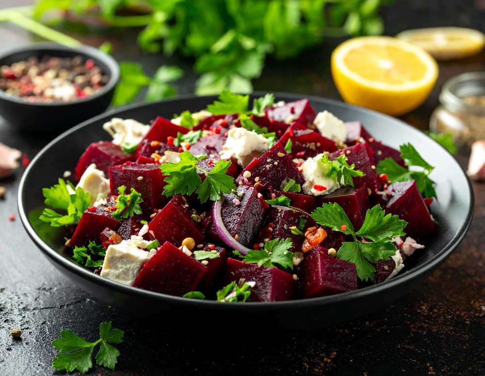 Beetroot salad with feta cheese top with parsley, serve in a black bowl with a side of lemon, top close-up view.