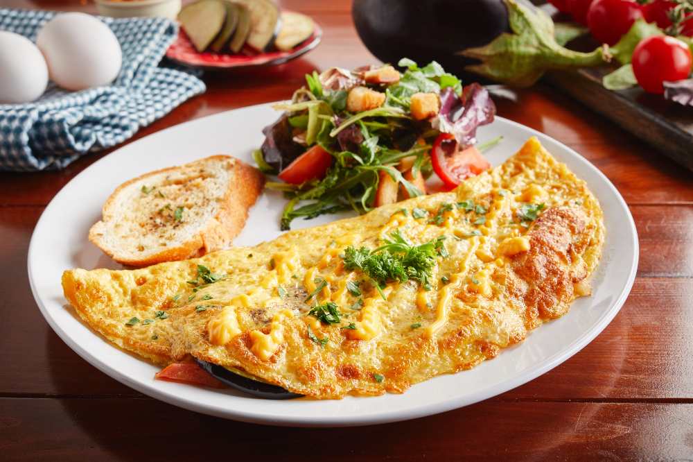 Eggplant omelette with side salad and bread served in a white plate on wooden table.