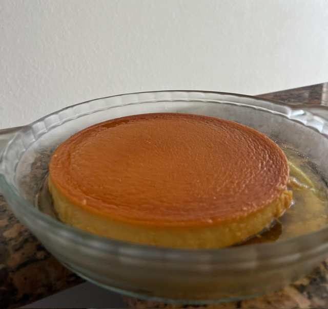 Flan serve in a round clear oven dish, on top of a kitchen counter, close-up top view.