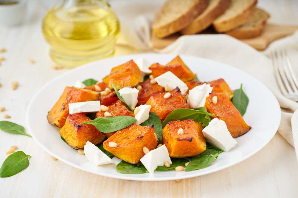 Salad with roasted pumpkin, feta cheese, spinach, nuts with honey and seasonings, close-up side view, with olive oil and slice bread on the side.