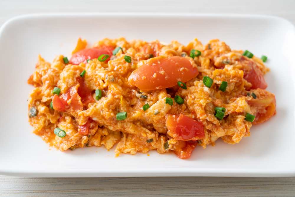 Scrambled eggs with tomatoes serve on a withe plate topped with green onion, top close-up view