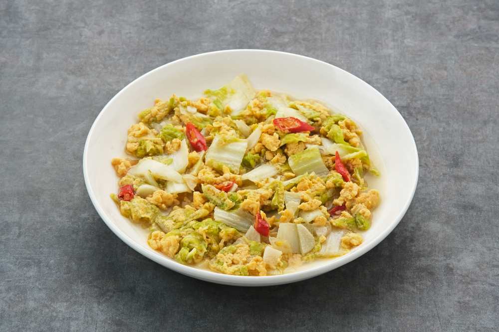 Tumis Sawi Telur or stir fry egg cabbage, Indonesian food, serve in a white bowl, on a gray rustic table. top view