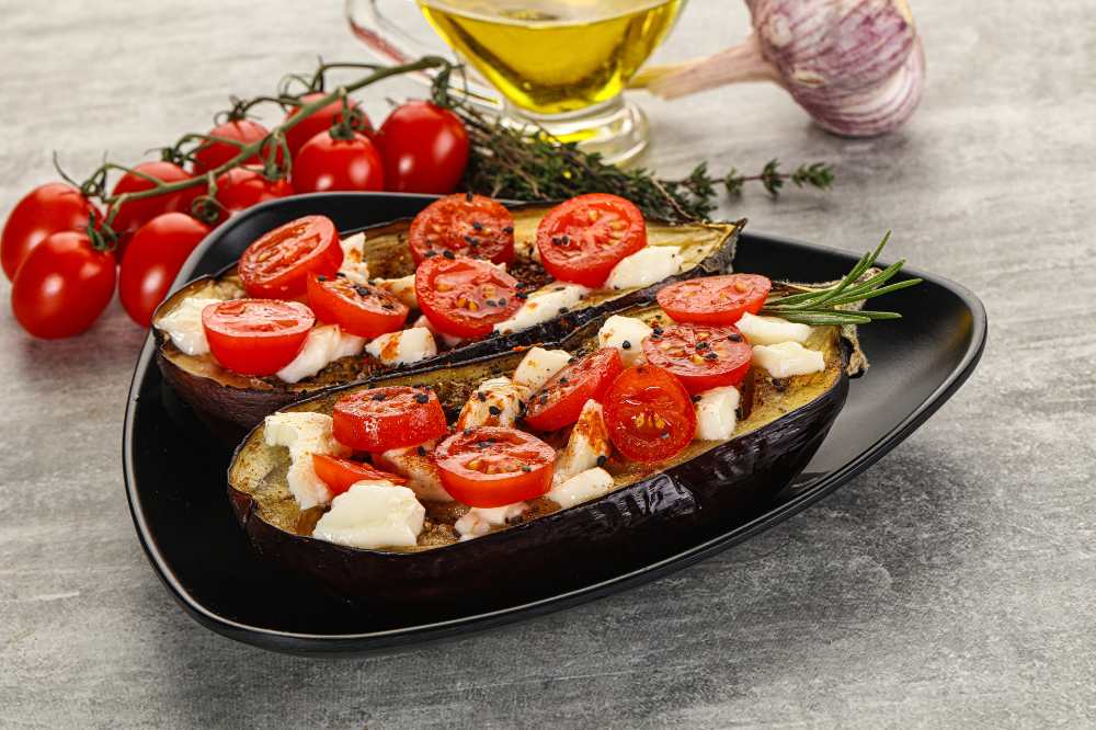 baked eggplant with feta and cherry tomato, serve on a black plate, with a side of cherry tomato olive oil and fresh garlic, on a rustic gray counter.