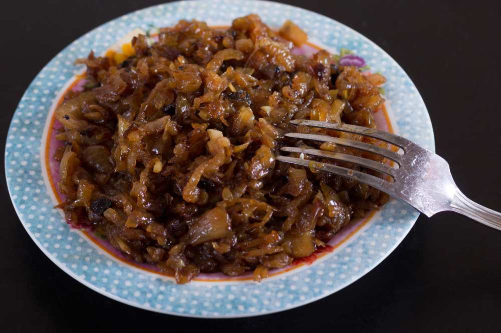 caramelized onion on a decor blue plate with fork, on a black background, close-up side view.