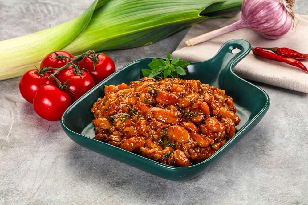 chili with tomatoes , Garlic and leak onions, serve on a green pan, with fresh tomatoes, garlic, chili, leak on the side.