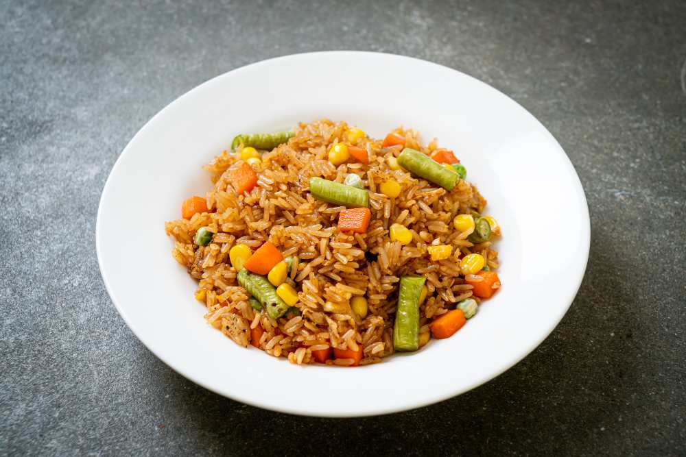 fried rice with green peas, carrot and corn, serve in a white plate on a rustic gray table, top view.