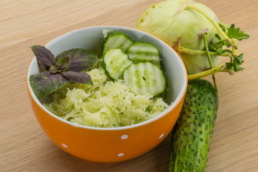 kohlrabi, Cucumber salad, serve in an orange bowl, with fresh kohlrabi and cucumber, on a wooden counter.
