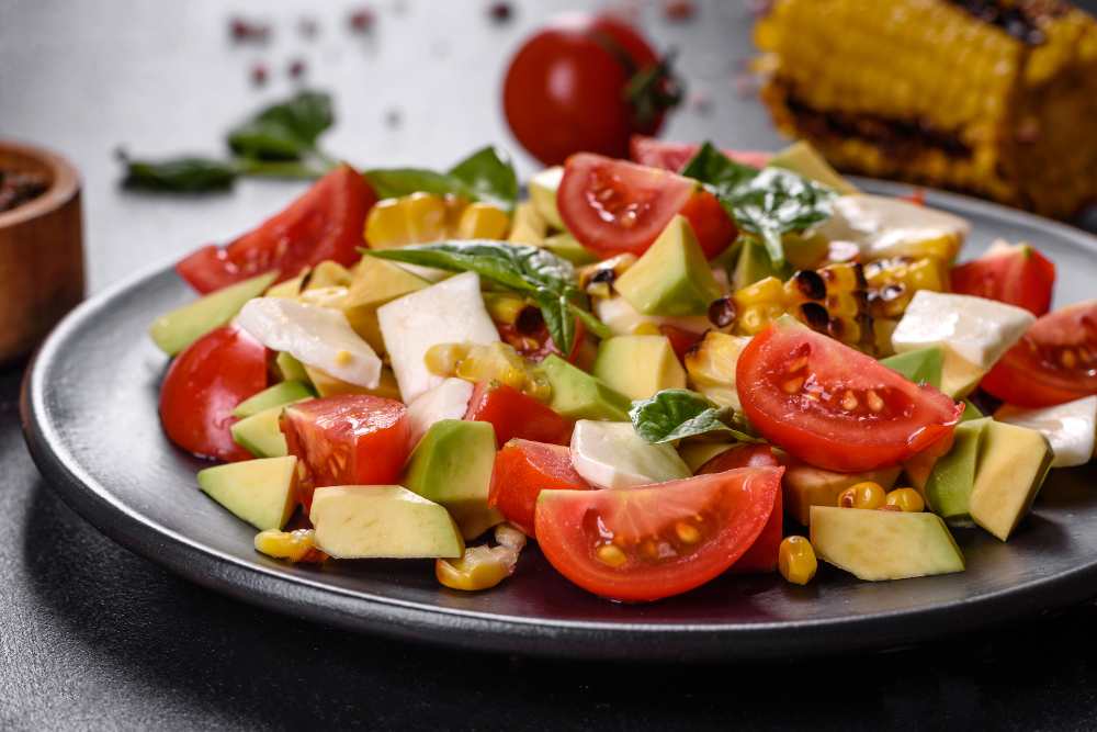 salad with tomatoes, avocado, Feta cheese and grilled corn top with Basil, serve in a rustic black plate., with tomato and corn on the side.