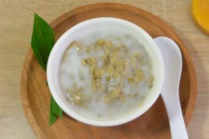 Mung Bean Porridge or Bubur Kacang Hijau, Indonesian dessert, serve in a white bowl on a wooden plate with white spoon on the side, close-up top view.