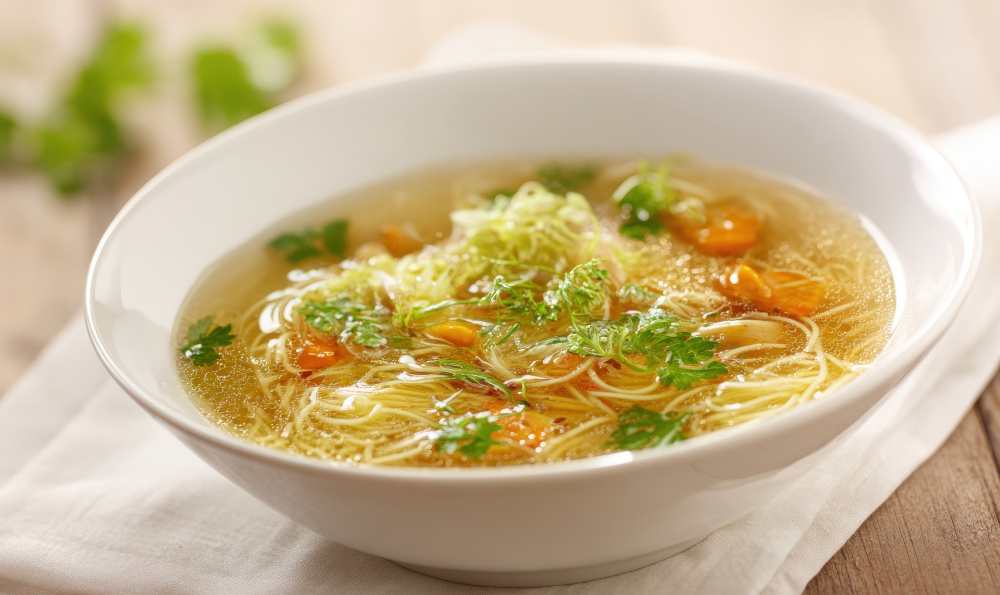 Noodle soup with vegetables and herbs, serve in a white bowl on a white napkin, a close-up top view.