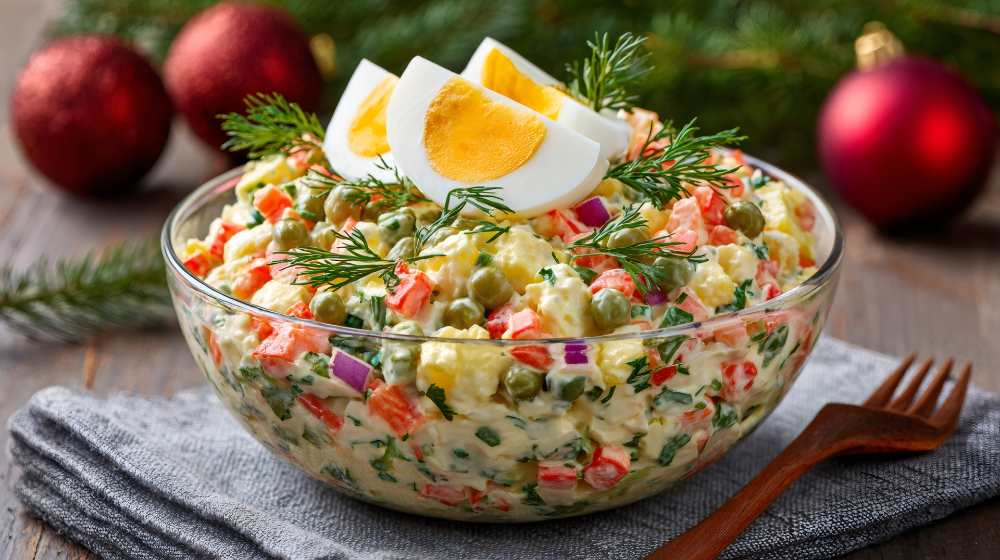 Olivier salad with eggs serve in a clear glass on a wooden table, a close-up side view.