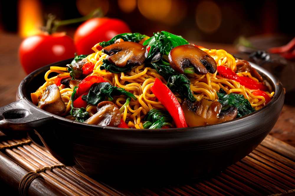 Stir-fry noodles with red peppers spinach, and mushrooms, serve in a black bowl, with whole tomato on the side, close-up side view.