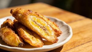 Thai fried banana, banana fritters , serve in a small white plate on a wood countertop table, close-up side view.
