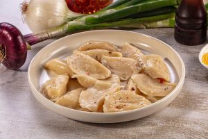 Vareniki dumplings with onions and spices, serve in a white bowl on a rustic table, with fresh onion on the side. close-up top view.