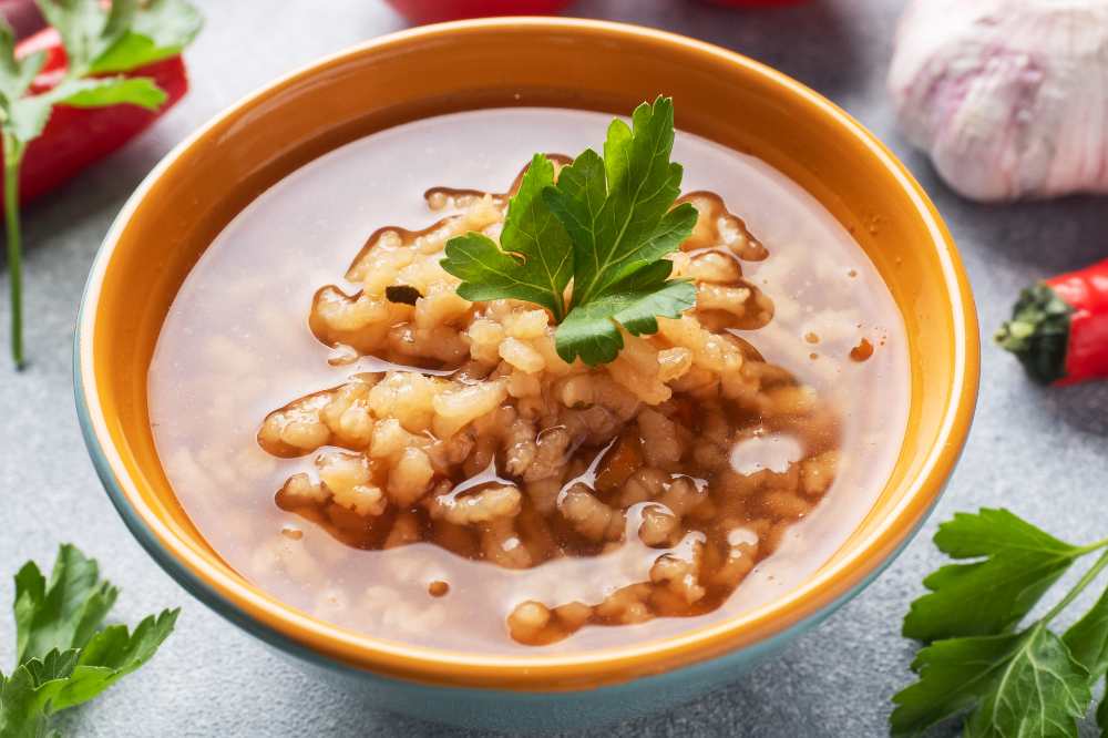 Vegetarian soup kharcho with rice and vegetables. Garlic hot pepper tomatoes. serve in a rustic yellow bowl, close-up top view.