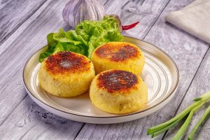fried cornmeal patties with side of lettuce and fresh garlic serve on a plate, with fresh garlic and green onion , on a rustic wooden table, close-up side view.
