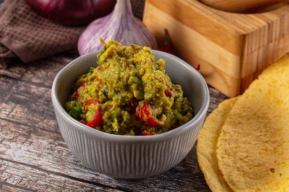 guacamole dip with fresh avocado, tomato, and cilantro, serve in a gray cup with whole fresh garlic on the side, close-up top view.