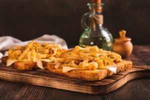 open face toast with melted cheese and caramelized onions, serve on a wooden cutting board with side of olive oil, close up side view.